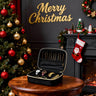 Black jewelry case with gold jewelry on a wooden table in front of a Christmas tree and fireplace.
