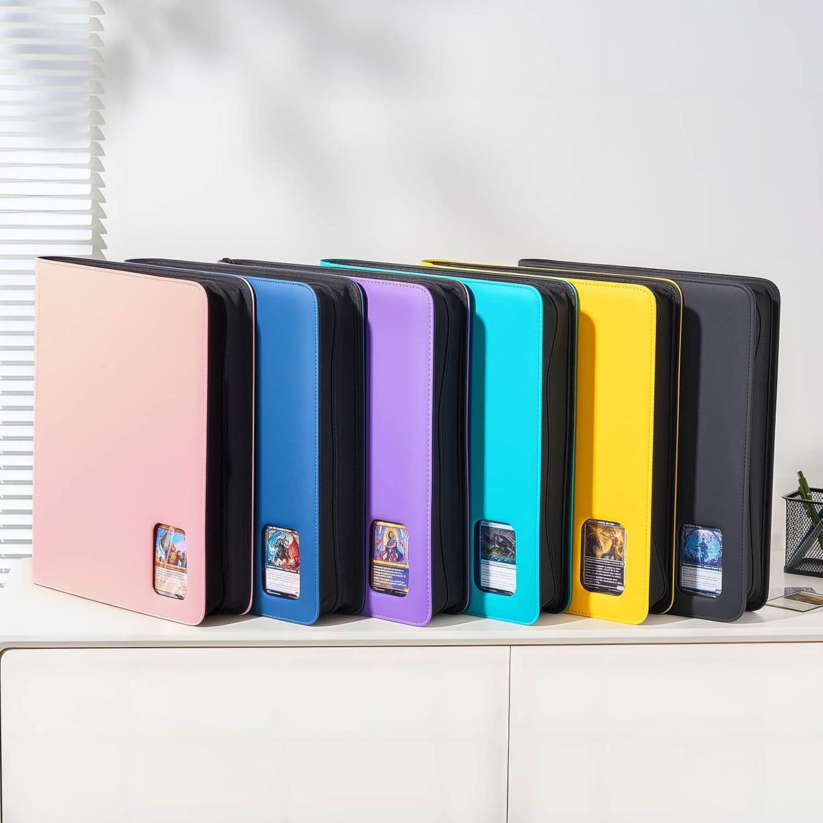 Six colorful card sleeves or portfolios in pink, black, blue, purple, teal, yellow, and dark gray, arranged side by side on a white cabinet.