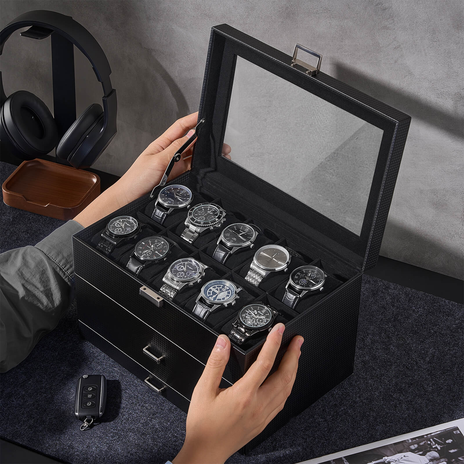 Person opening a black watch display case with multiple watches inside, on a dark surface.