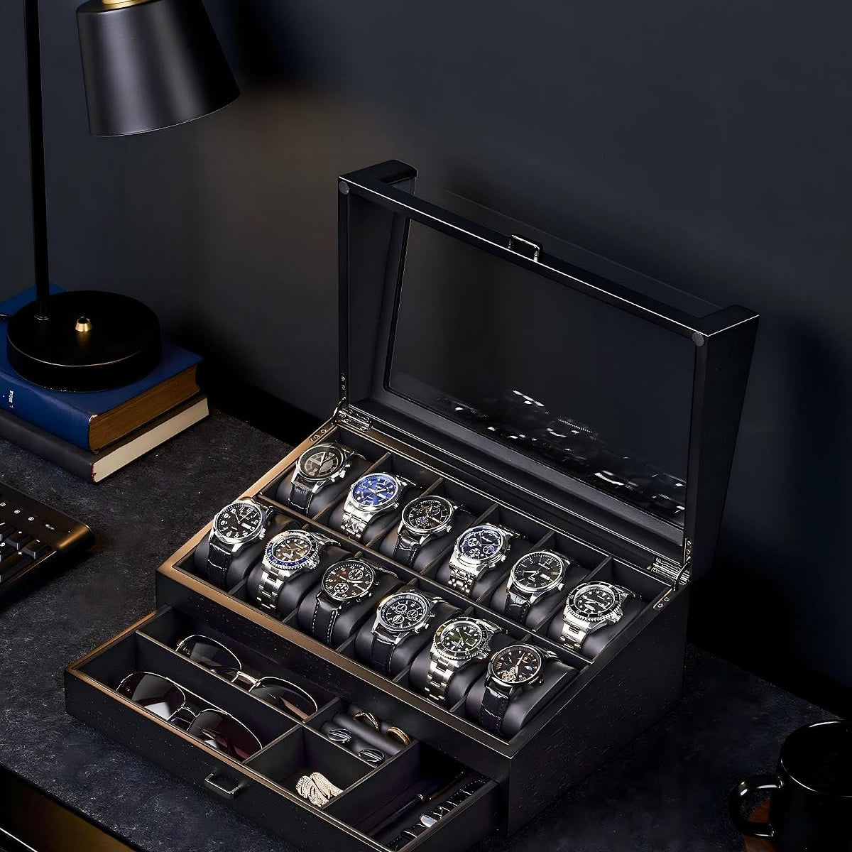 A black wooden watch winder box with a glass lid, shown open on a dark desk. 