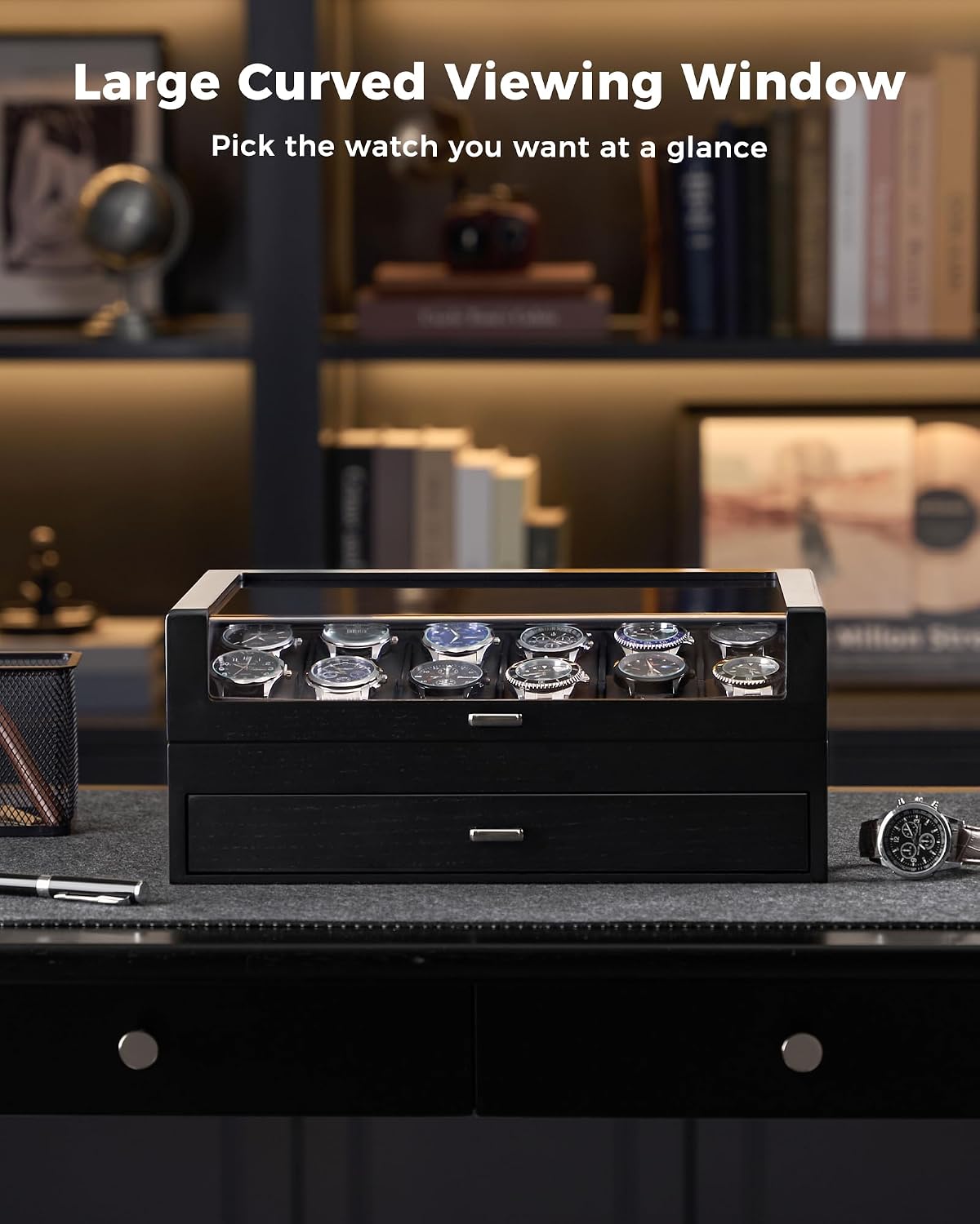 A black watch display box with a clear glass top window showing several wristwatches inside, placed on a dark desk in a dimly lit home office setting. 