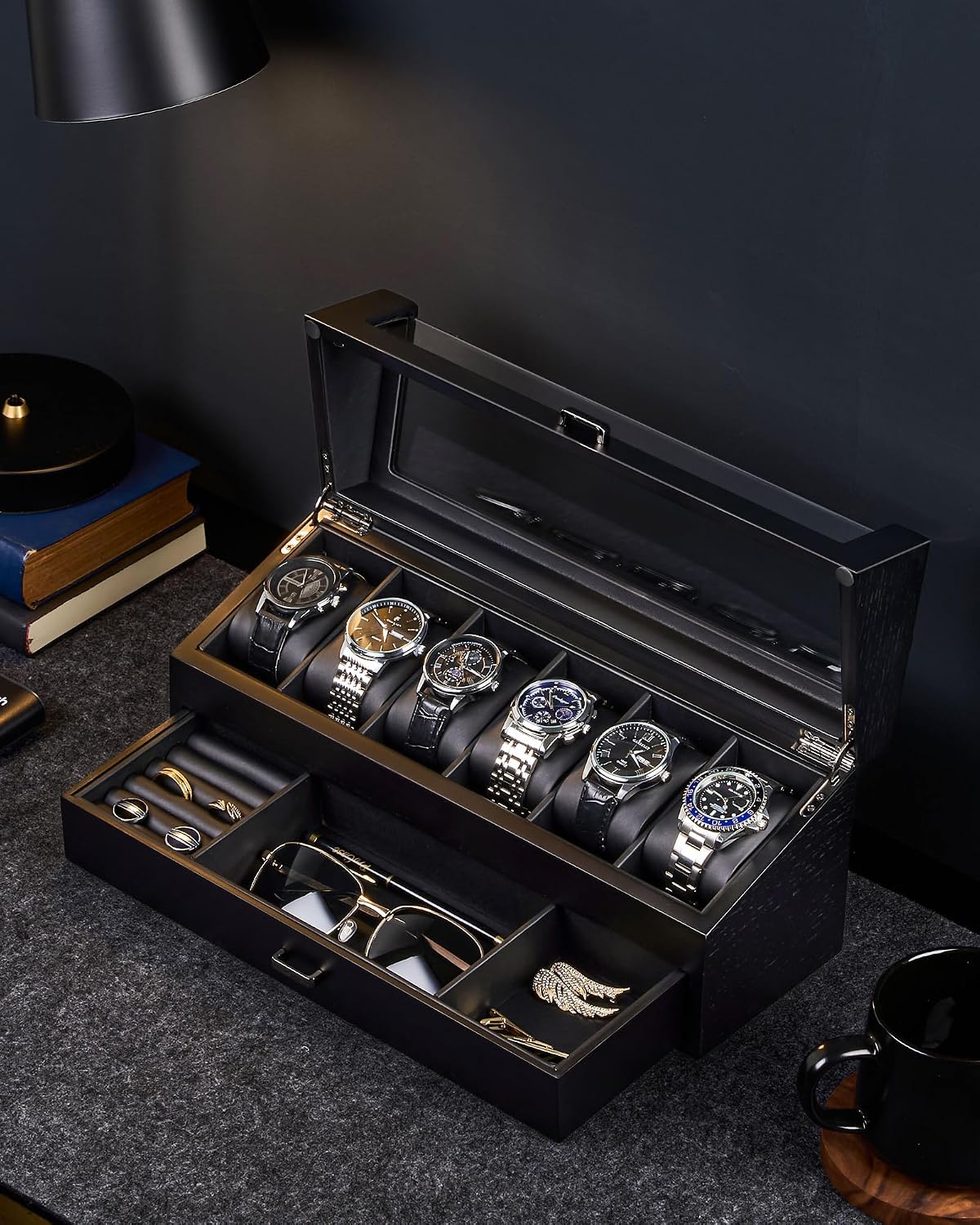 A black watch and accessory storage box with a glass top lid, shown open on a dark tabletop. 