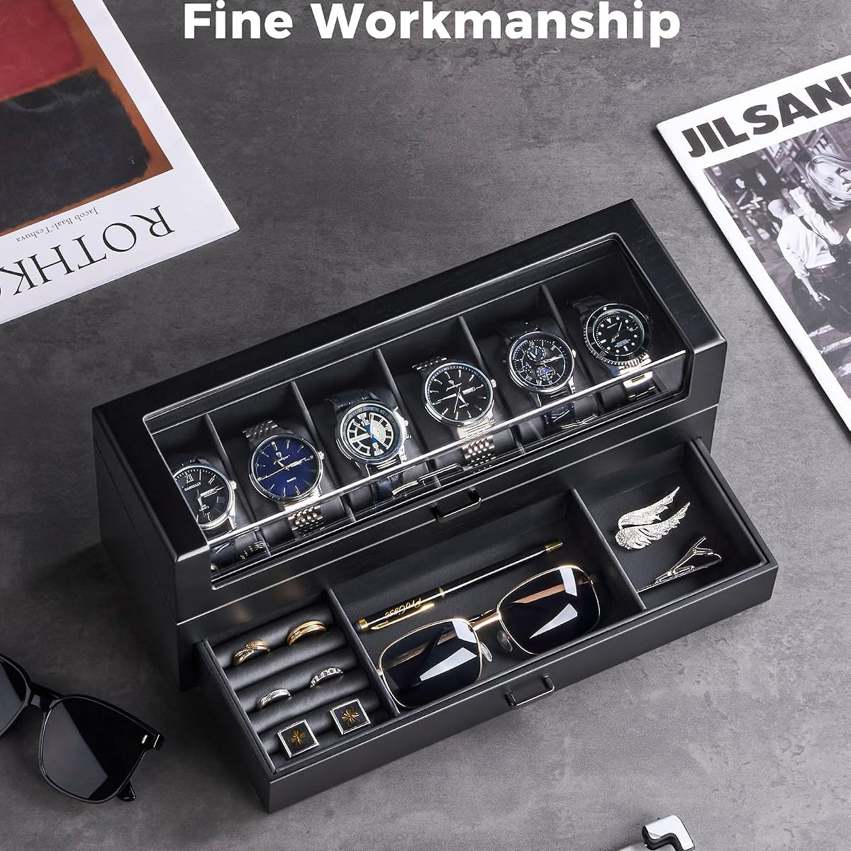 A black multi-compartment watch and accessory organizer box shown open, with several wristwatches in the top and small jewelry pieces in the drawer.