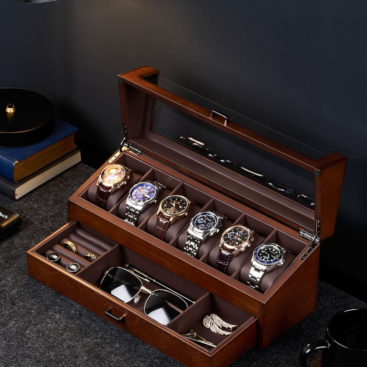 A wooden watch storage box with a glass lid, shown open on a dark tabletop. 