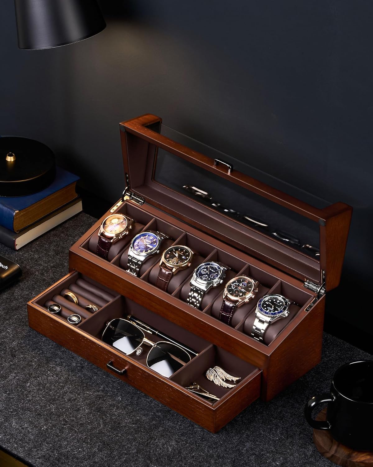 A wooden watch storage box with a glass lid, shown open on a dark tabletop. 