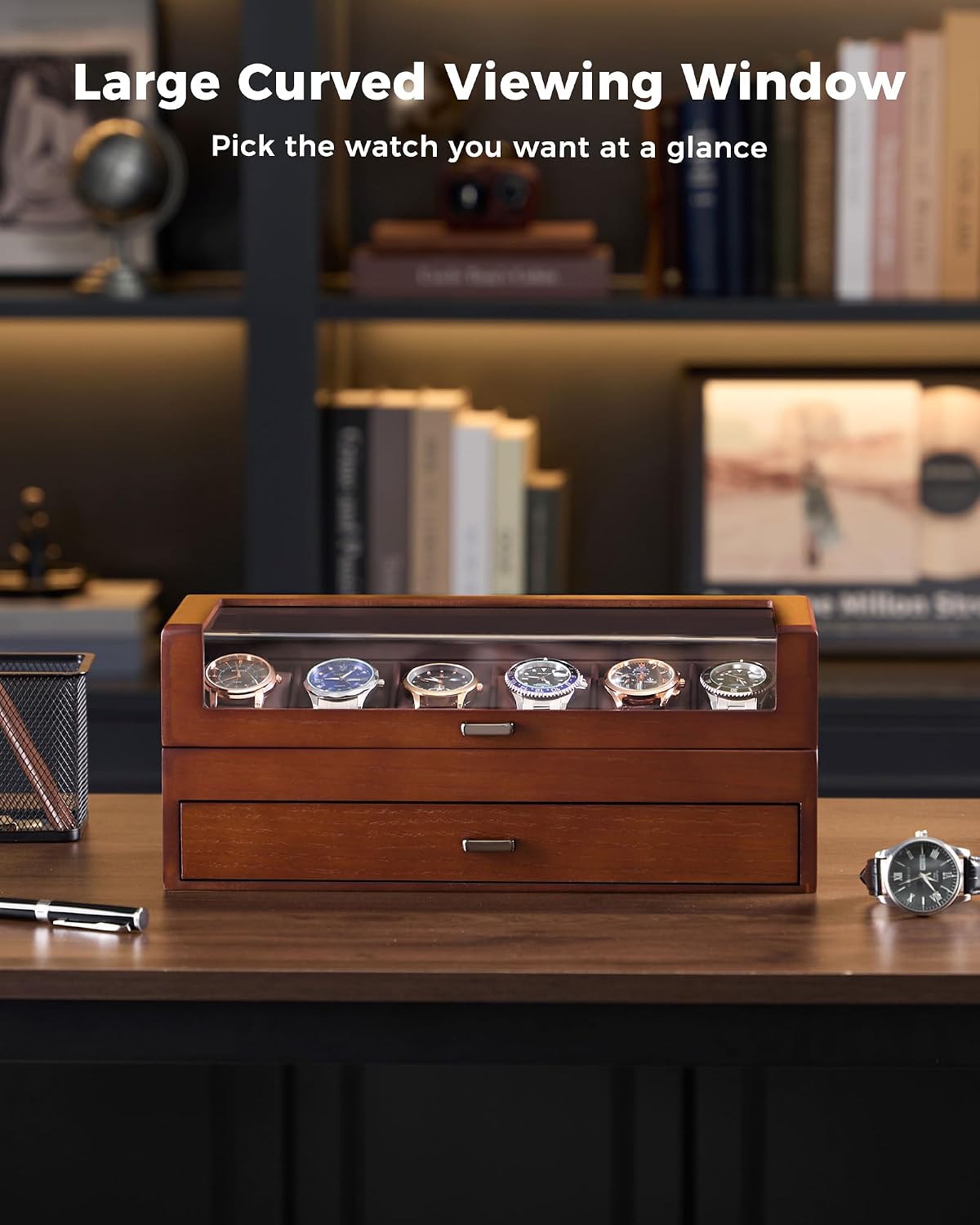 A wooden watch display box with a glass top window showing several watches inside, placed on a desk in a blurred office setting. 
