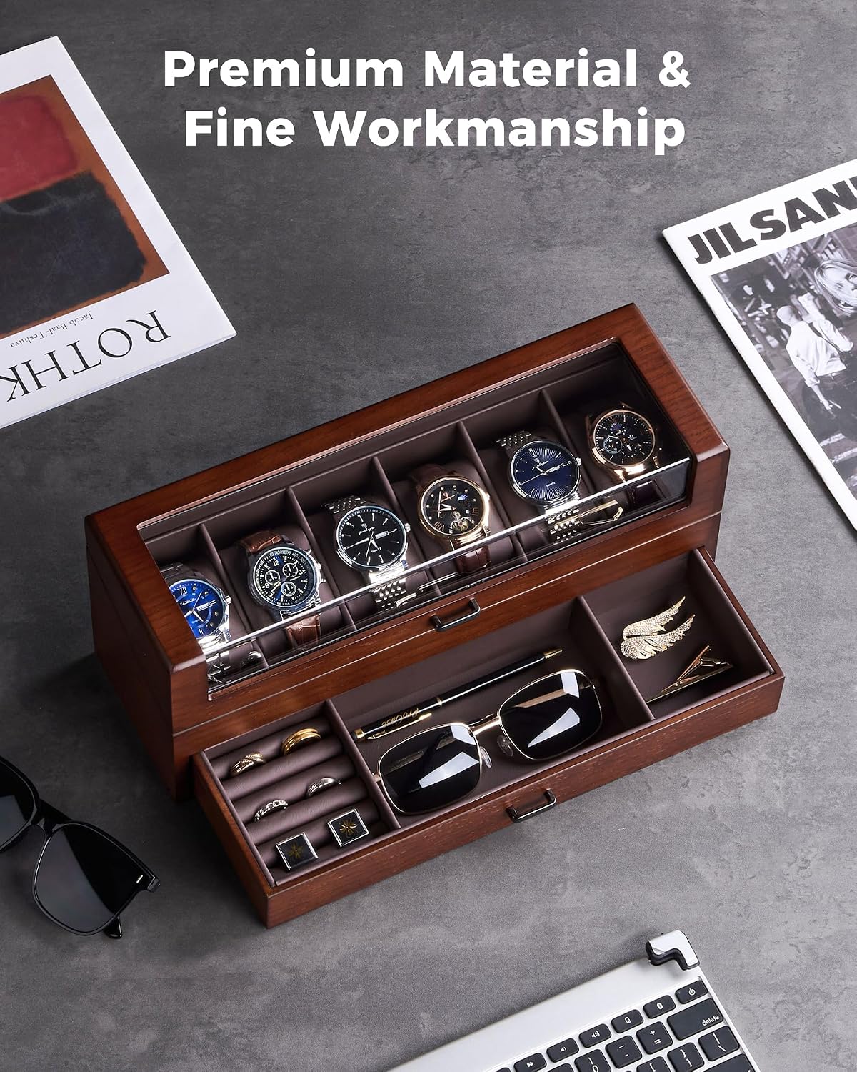 A premium wooden watch and accessory organizer with a top watch display and an open drawer holding sunglasses, cufflinks, and a tie, styled on a gray surface with magazines and a laptop nearby. 