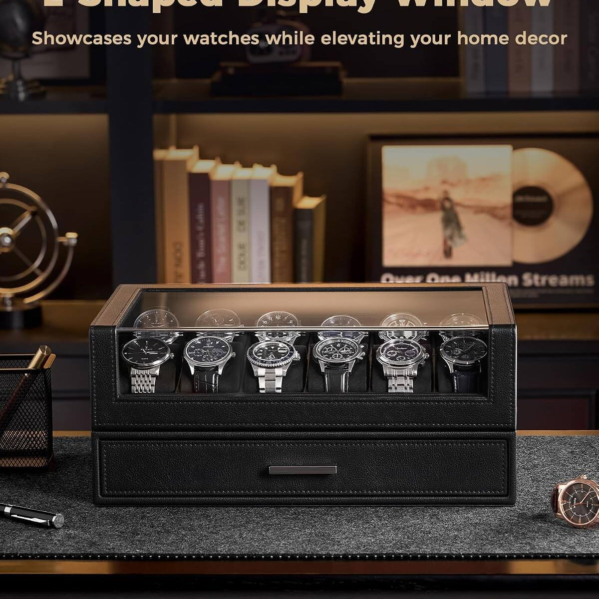 A black L-shaped watch display box with a glass top window, shown holding six wristwatches on a dark desk in a styled home office setting. 