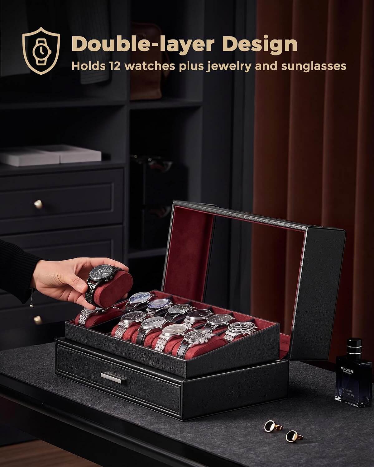 A black double-layer watch storage box with a red interior is shown open on a dark table, holding several watches and jewelry. A hand is placing a watch into the top compartment.