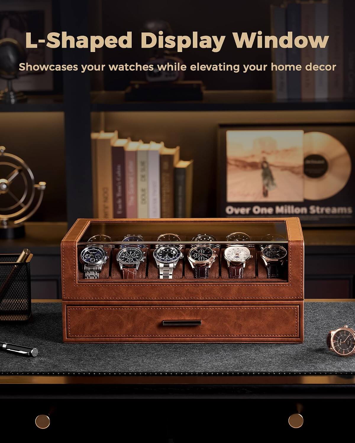 A brown leather watch display box with a glass top window, shown holding multiple wristwatches on a dark desk. The scene is styled in a home office setting with books, a record player, and shelves in the background