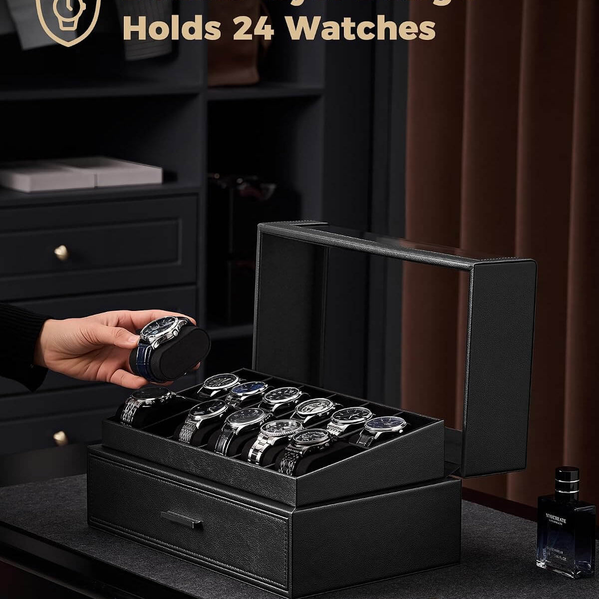 A black watch box with a  lid is shown open on a dark table, holding multiple watches inside. A hand is placing a watch into the box.