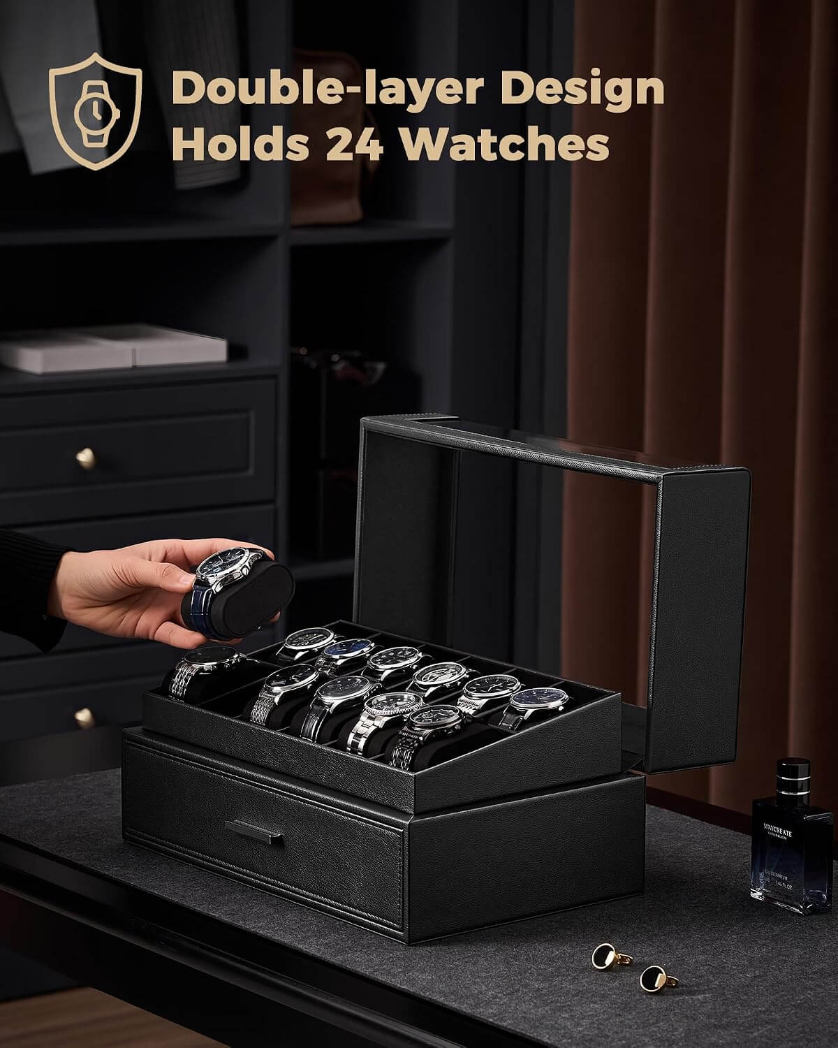A black watch box with a  lid is shown open on a dark table, holding multiple watches inside. A hand is placing a watch into the box.