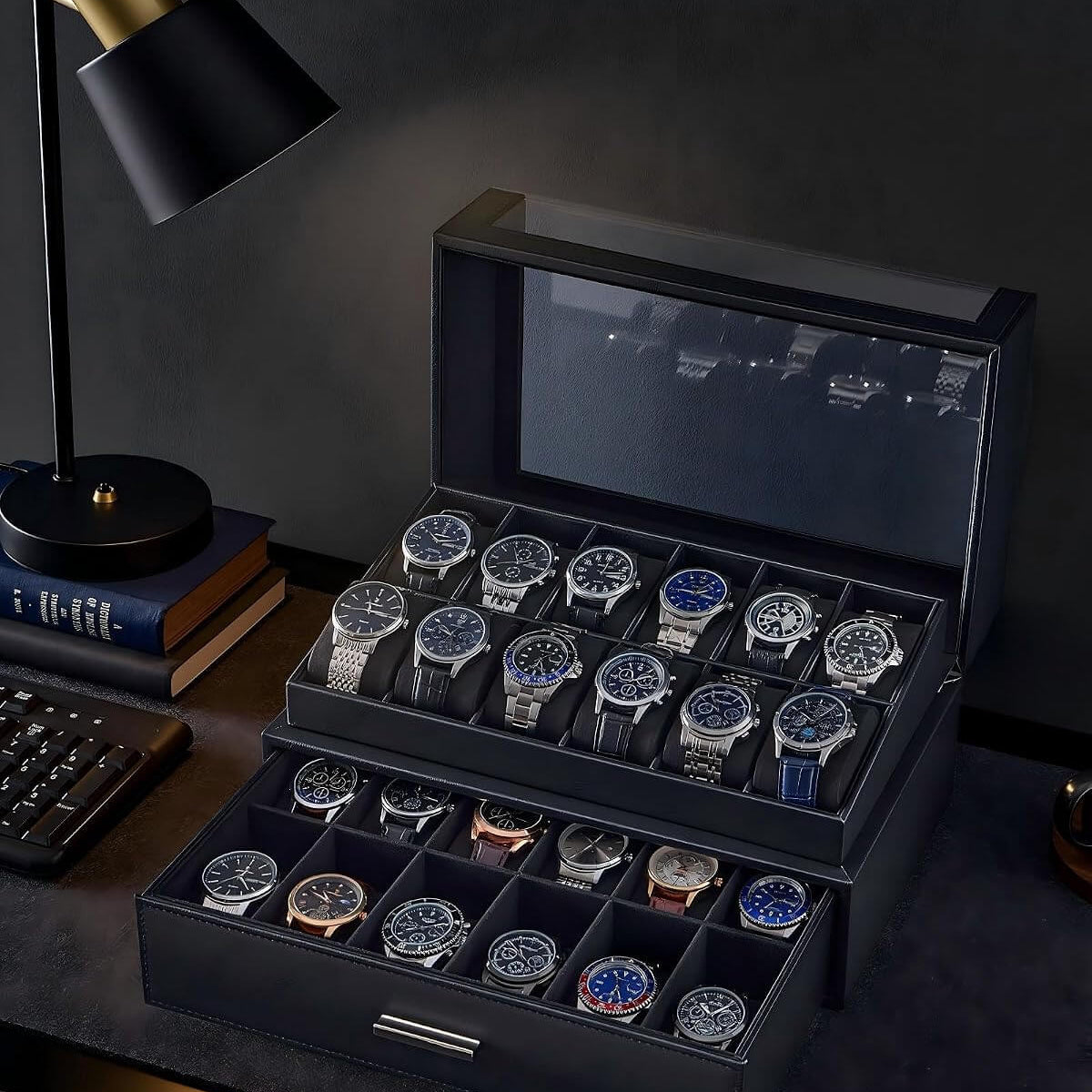 A black watch storage box with a  lid, shown open on a dark desk. The box contains multiple rows of wristwatches in divided compartments