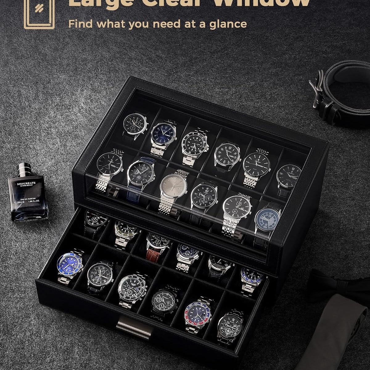 A black watch storage box with a clear top window and an open lower drawer, shown on a dark textured surface with several watches inside.