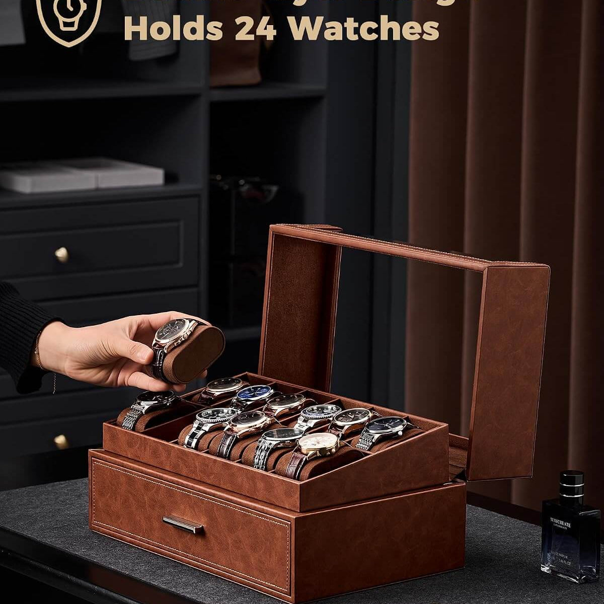 A brown leather watch storage box with a glass top window, shown open with multiple watches stored inside. A hand is placing a watch into the box.