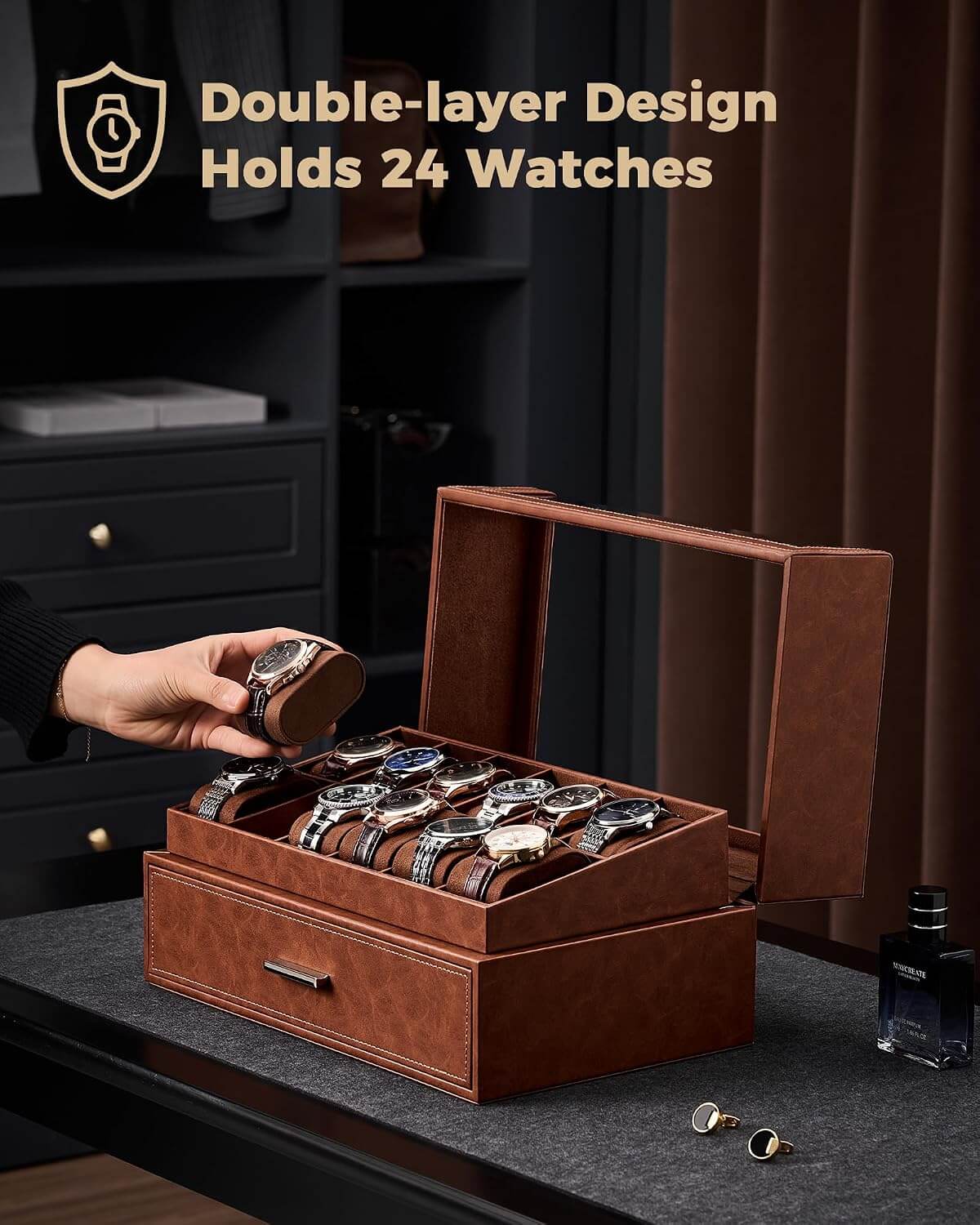 A brown leather watch storage box with a glass top window, shown open with multiple watches stored inside. A hand is placing a watch into the box.