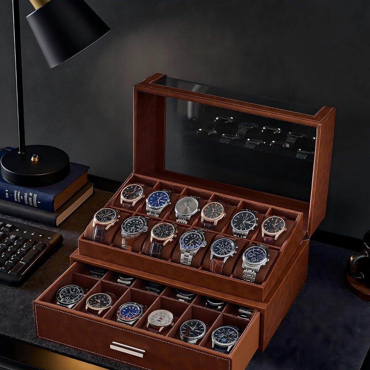 A brown watch display case with a glass top, shown open on a dark desk. The case contains multiple rows of wristwatches, and a matching drawer sits below.