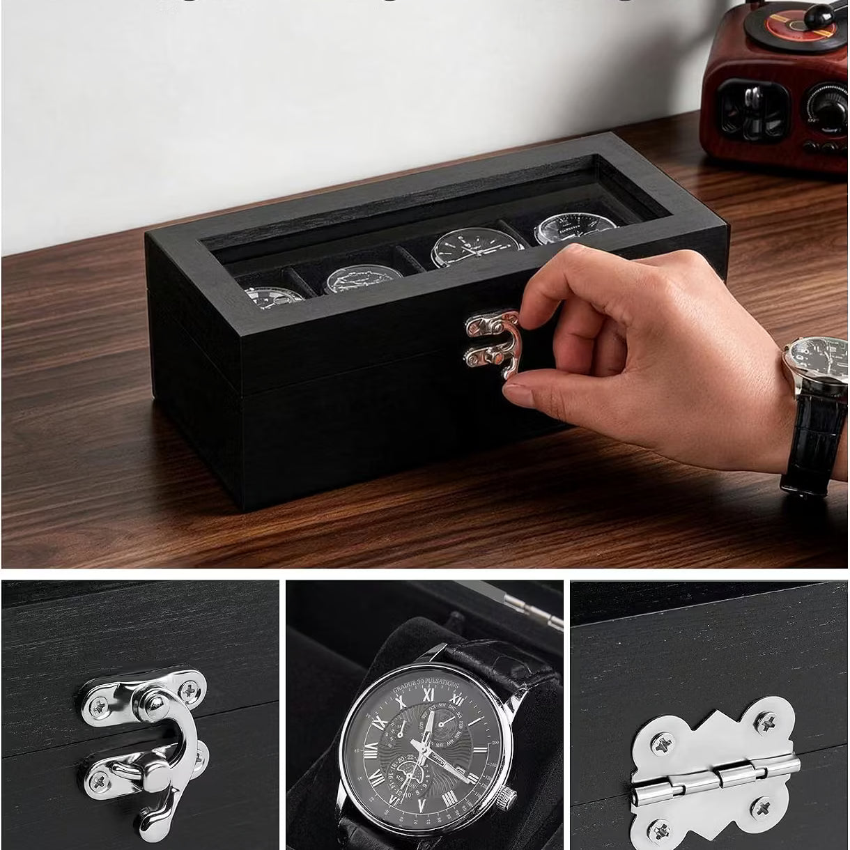 A black wooden watch display box with a transparent top and three watch slots, shown on a dark wood tabletop. A hand is opening the front latch.