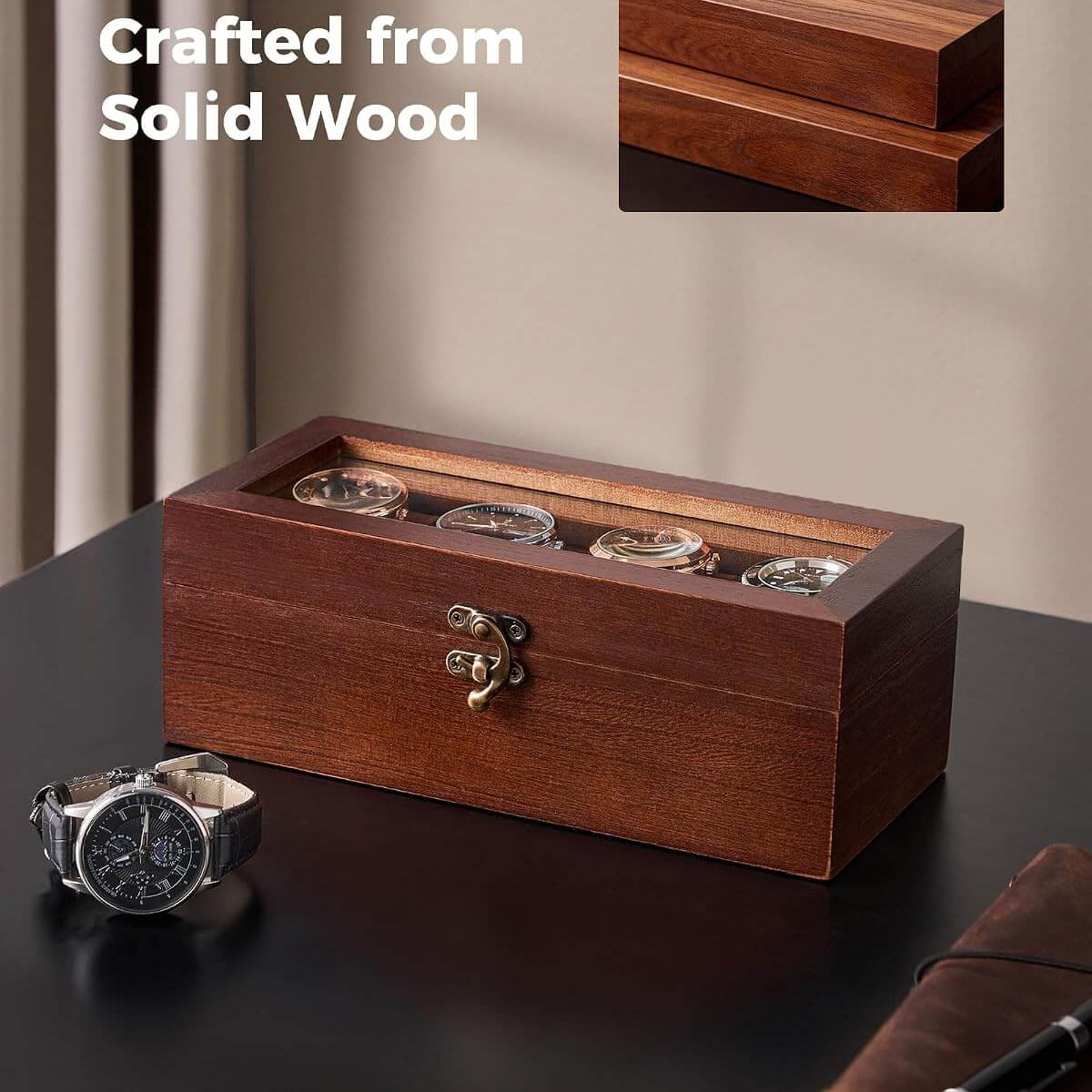 A rectangular wooden watch box with a transparent top and four visible watch faces, placed on a dark tabletop. A wristwatch and a notebook are nearby as props, and the text 'Crafted from Solid Wood' appears in the upper left with a small inset showing the wood grain detail.