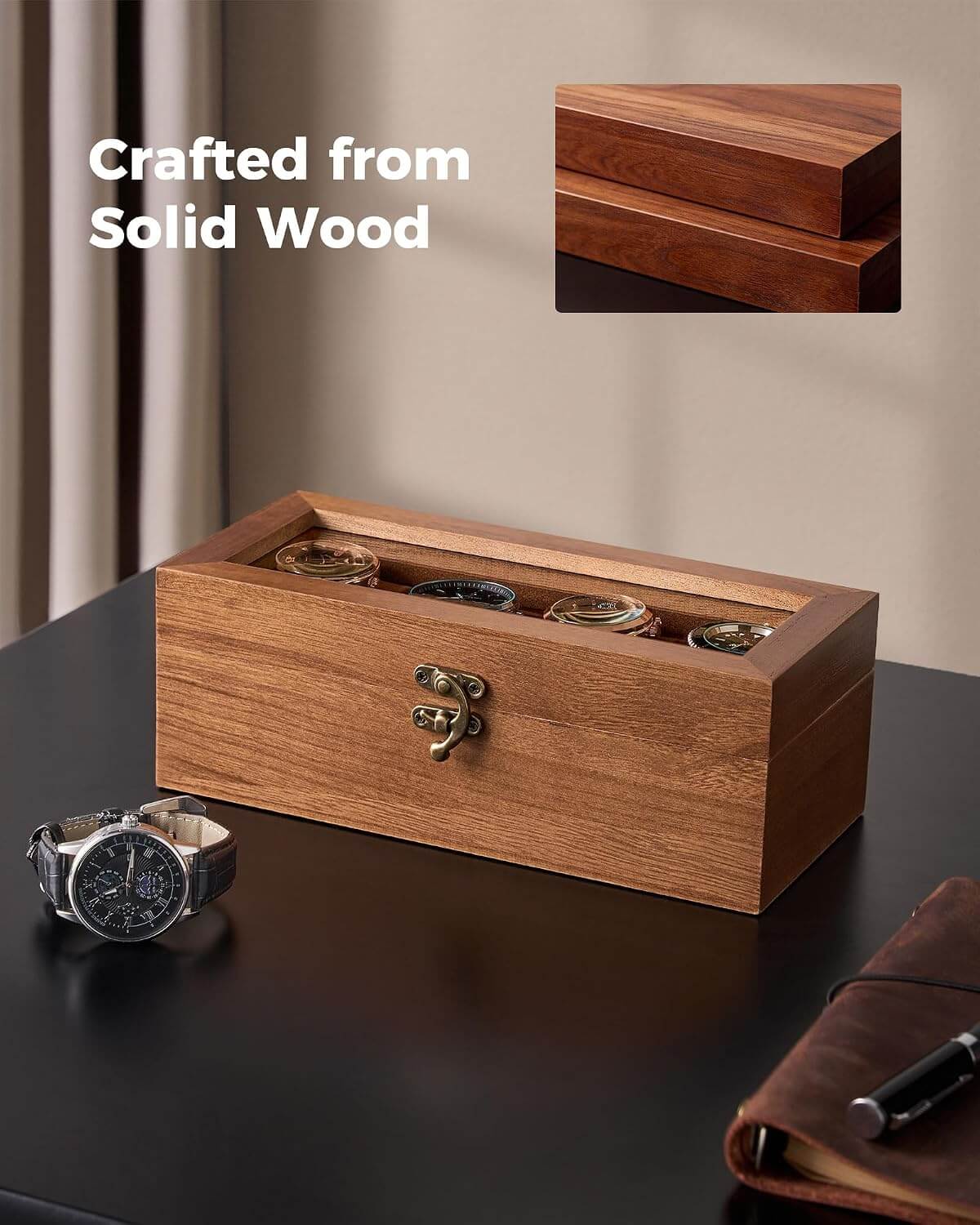 A rectangular wooden watch box with a transparent top, shown on a dark tabletop in a styled indoor setting. Several watches are stored inside, and a small inset at the top right shows a close-up of the wood grain.