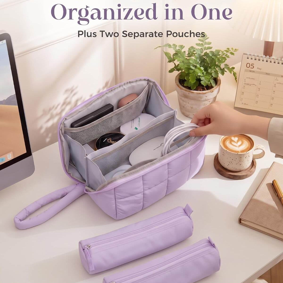 A lavender puffy tech pouch shown open on a desk, with two separate matching pouches placed in front. A hand is placing a white cable into the bag's interior compartments.