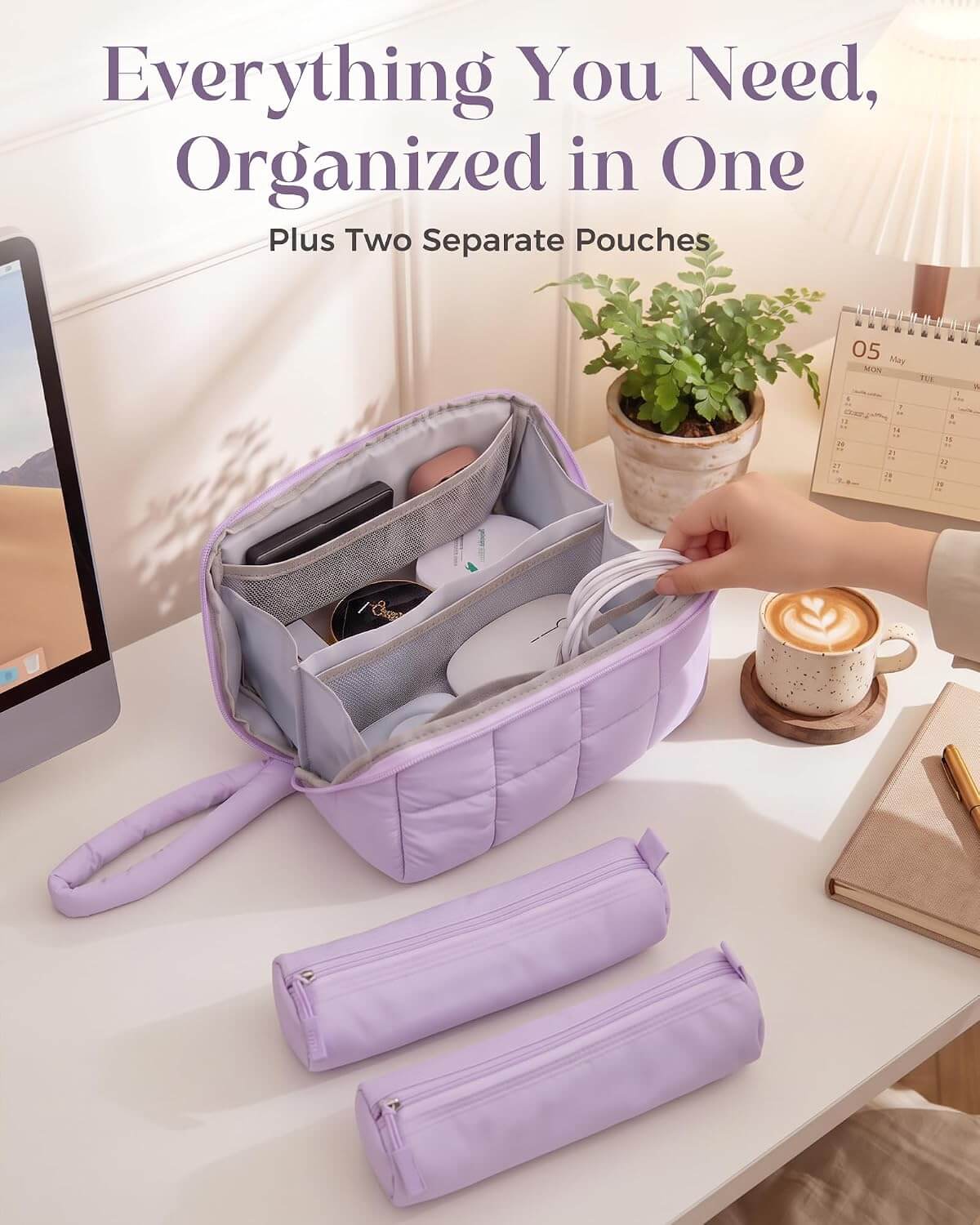 A lavender puffy tech pouch shown open on a desk, with two separate matching pouches placed in front. A hand is placing a white cable into the bag's interior compartments.