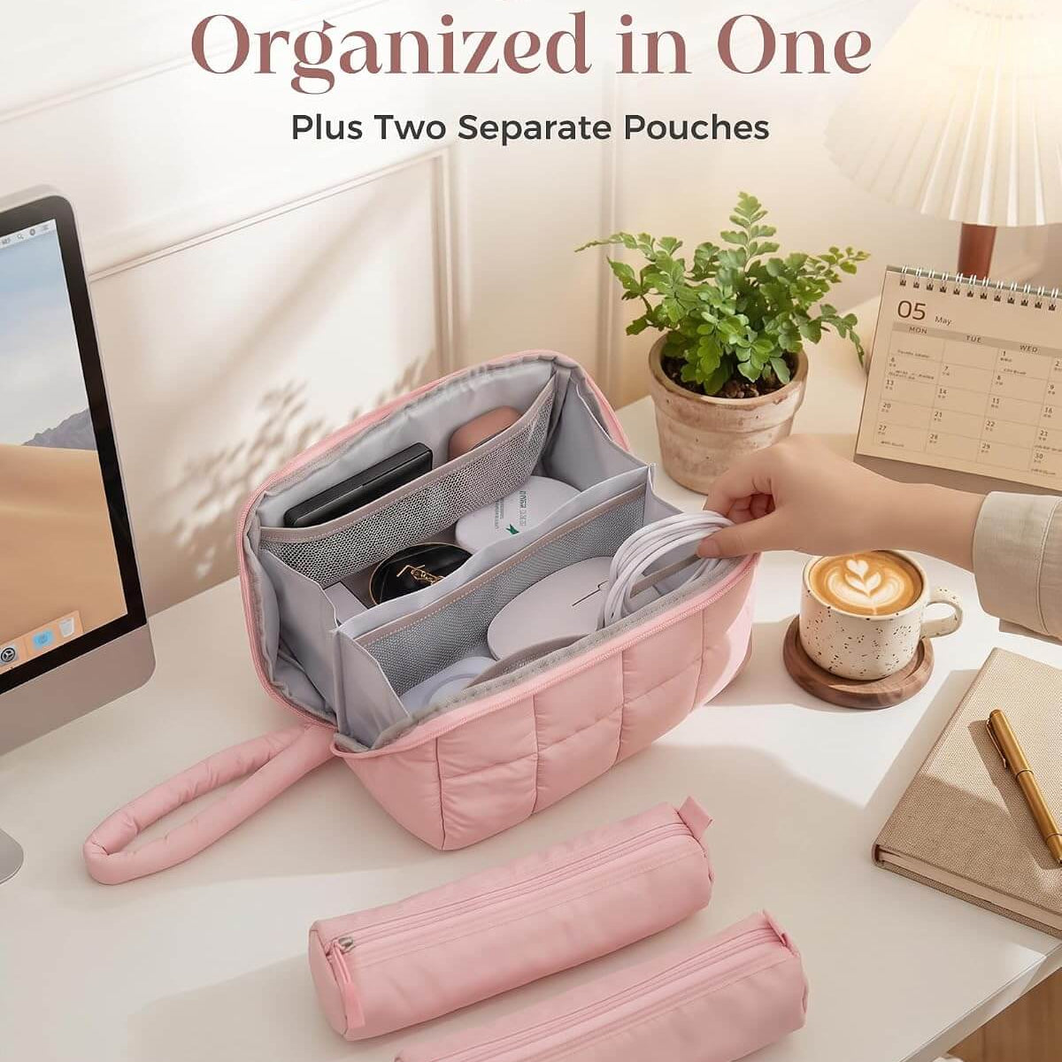 A pink puffy tech pouch with a hand strap is shown open on a desk, containing phone accessories and other small items. Two matching pink zip pouches are placed in front, and a hand is placing items into the main bag.