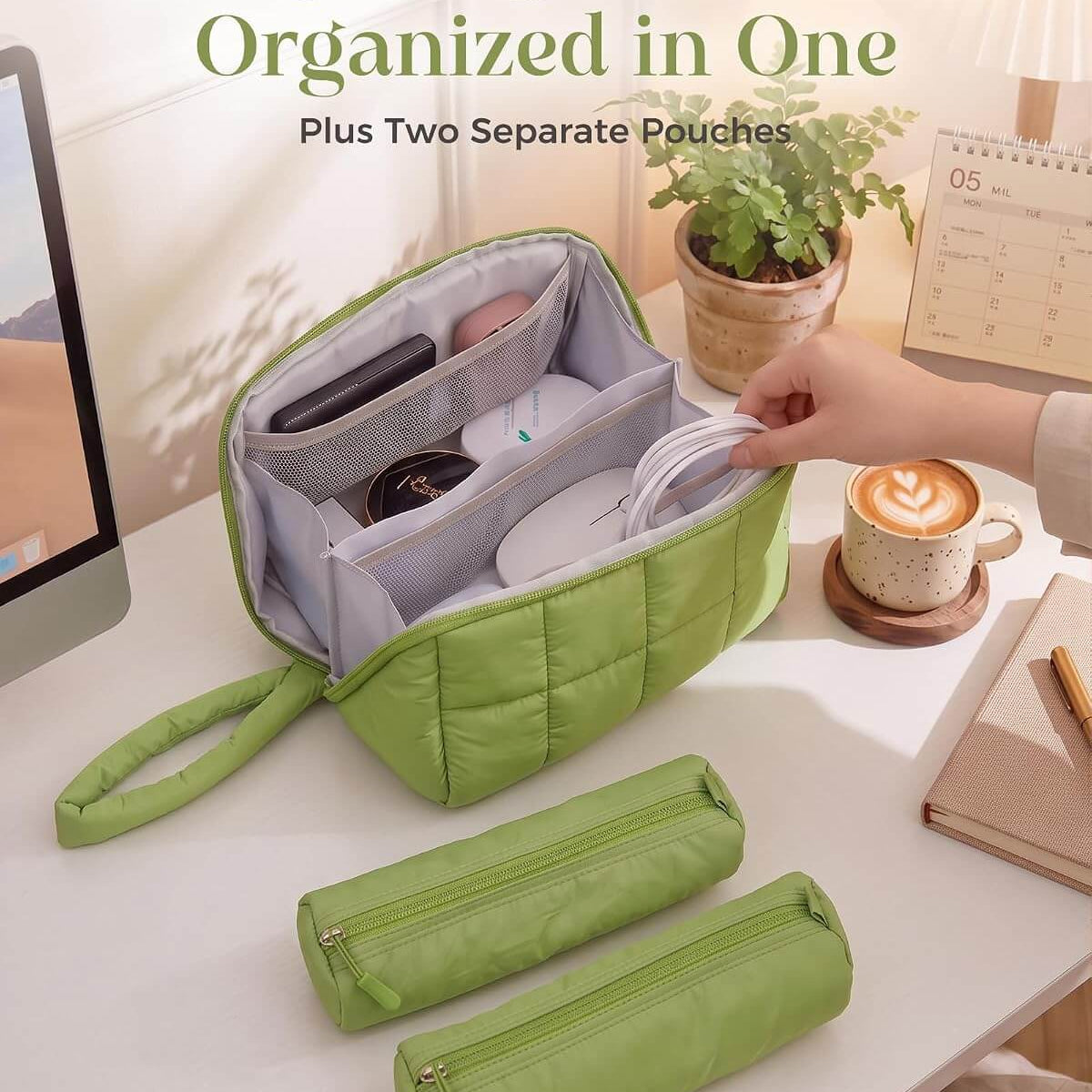 A green puffy tech pouch with multiple interior compartments, shown open on a desk with a hand placing a white cable inside. Two matching zip pouches are placed in front, and a hand is visible reaching in.