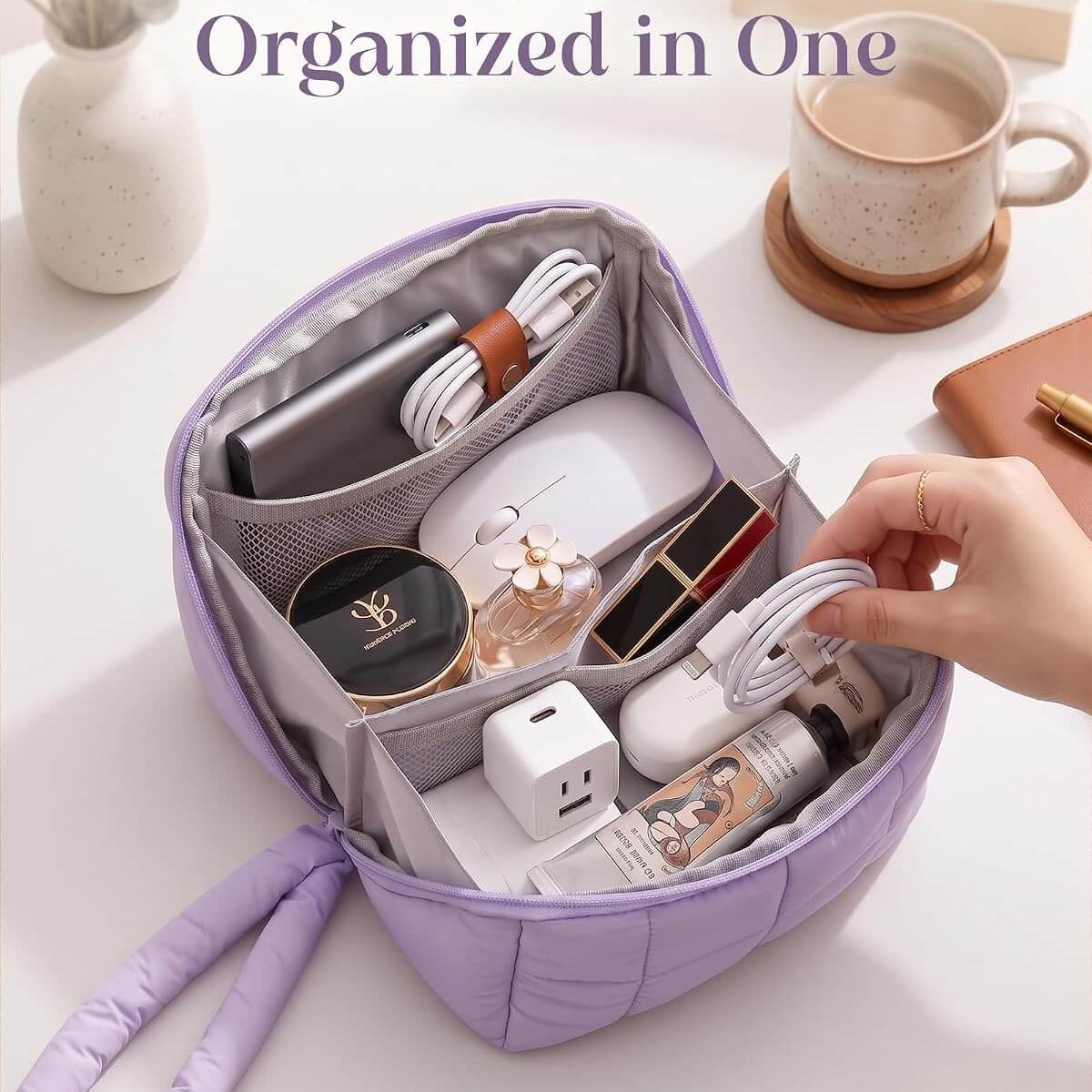 A lavender puffy tech pouch with a handle, shown open on a white desk and filled with various personal items. A hand is holding a white cable inside the bag.