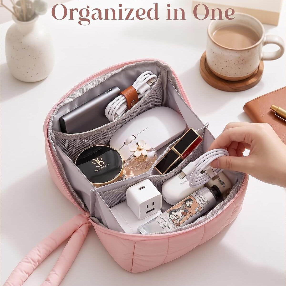 A pink puffy tech pouch with multiple interior compartments, shown open on a white desk with various personal items inside and a hand reaching in. The text at the top reads, 'Everything You Need, Organized in One.