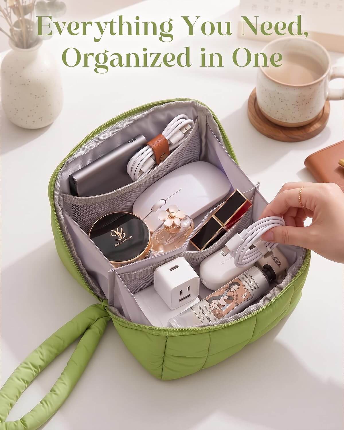 A green puffy tech pouch shown open on a white surface, filled with travel and beauty items. A hand is reaching toward the bag, and a coffee cup and vase are visible in the background.